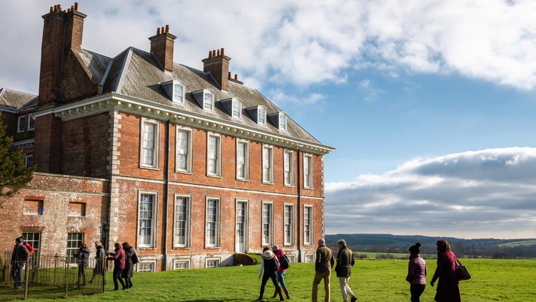 Visitors walking beside Uppark House, with countryside views and a bright autumn sky in the background.